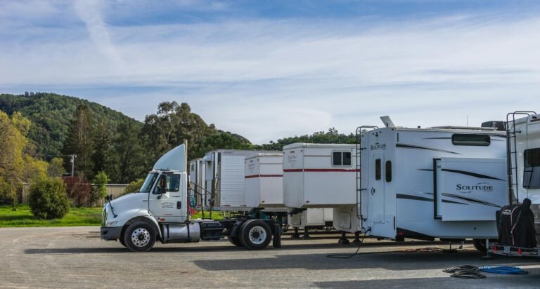 Trucks and RVs parked outdoors with trailers against a scenic mountain backdrop.